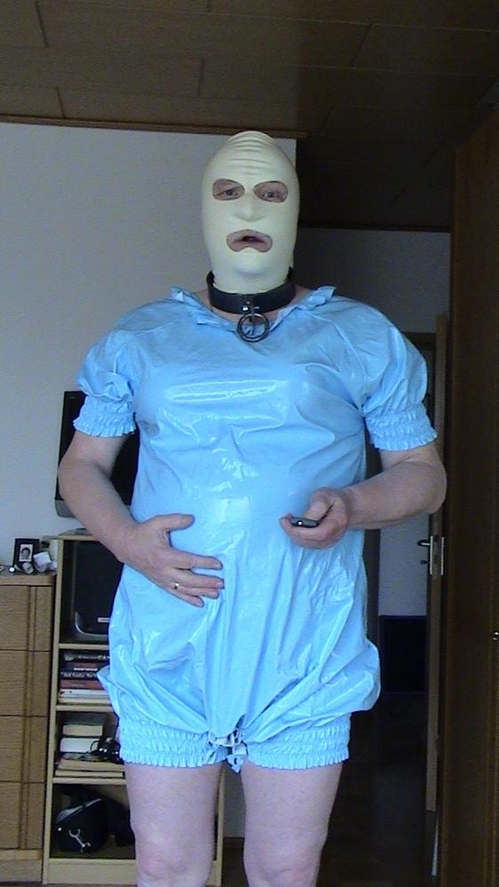 Babyslave mit Plastikspielanzug, Latexmaske und Halseisen
